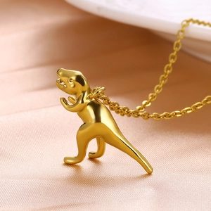 Polished gold dinosaur pendant necklace with sleek metal chain on orange silk background