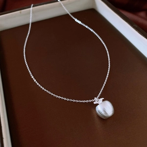 Détail macro du pendentif pomme en argent brossé dans son écrin à bijoux blanc