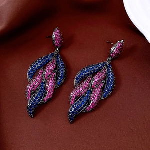 Detailed macro view of leaf-shaped earrings with blue and rose red crystals on dark metal