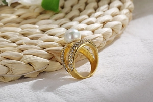 Macro detail of gold plated pearl ring featuring double layer cross design with pavé crystals
