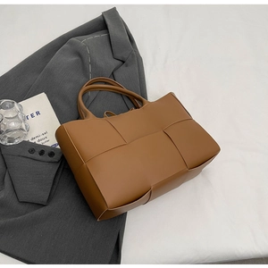 Detail of premium brown woven tote bag with textured straps on a stylish blazer background