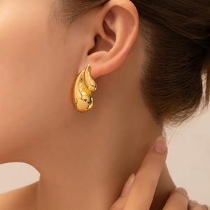 Detailed view of large gold-tone teardrop earrings with a polished metallic mirror finish