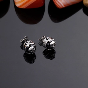 Macro shot of punk style silver skull earrings featuring a black faceted gemstone inlay