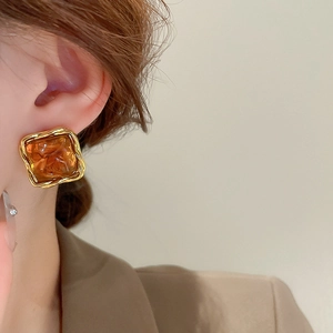 Close-up of geometric amber resin earring with gold twisted metal frame on model