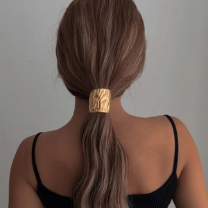 Golden hammer textured metal ponytail cuff accessory shown on a model's hair