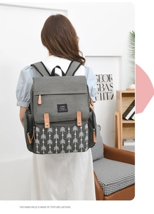 Rear view of a grey diaper backpack with brown leather straps and geometric arrow pattern