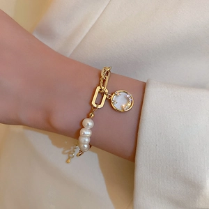 Close-up of freshwater pearl bracelet with gold chain and diamond smiley face charm on wrist