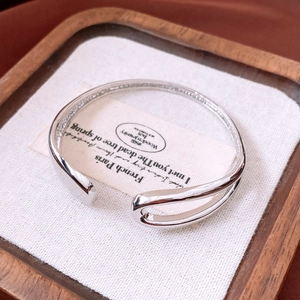 Detailed close-up of a minimalist silver open bangle with a hollow asymmetric metal design