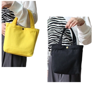Detail view of canvas tote bags in yellow and black featuring a metal snap button closure