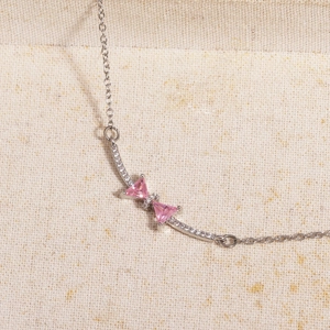 Close-up of pink bow necklace with triangle zircons and silver chain on textured fabric