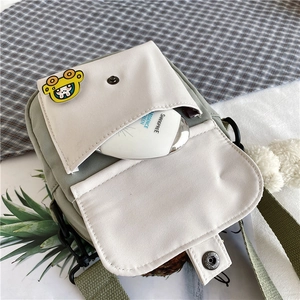 Détail du sac à bandoulière en toile crème et verte avec badges et sangle