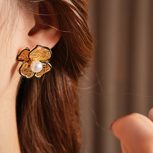 Detail of flower pearl stud earrings with woven metal texture on a female model