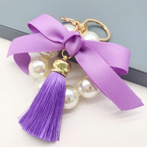 Macro detail of purple ribbon bow and pearl bead tassel keychain with golden metal clasp