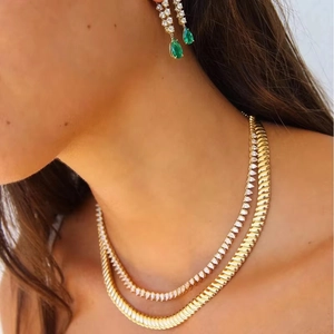 Detail shot of 10mm gold tennis chain layered with snake chain and emerald green earrings