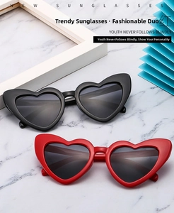 Detail of heart-shaped sunglasses in black and red on a white marble surface