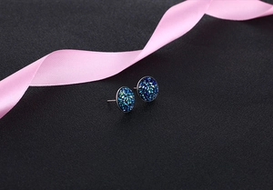 Macro shot of round S925 silver stud earrings with deep blue crystal druzy on black sand