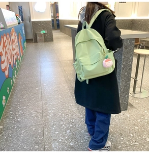 Nahaufnahme eines hellgrünen Nylon-Rucksacks mit einem süßen rosa Plüsch-Fruchtanhänger
