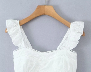 Détail d'un top court blanc brodé avec bretelles à volants sur un cintre en bois