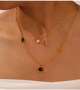 Detail of layered gold necklaces with bow pearl pendant and green gemstone on a model