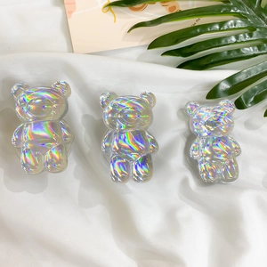 Close-up of holographic bear-shaped folding cell phone stands on white fabric