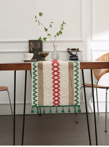 Detail view of cotton linen table runner with red diamond pattern and green tassels