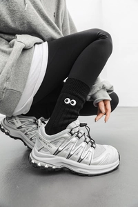 Detail of black knitted slouch socks with white eye embroidery and silver sneakers