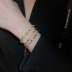 Close-up of three-piece stacked gold bracelets with multi-colored crystals on a black sleeve