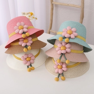 Detail of woven straw sun hats for kids featuring 3D fabric flowers and yellow ribbons