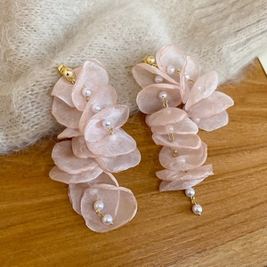 Close-up of elegant chiffon flower earrings with pearls and long tassel on wood