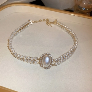 Détail d'un collier de perles double épaisseur avec pendentif fleur doré et strass brillants