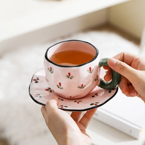 Close-up of pink floral ceramic coffee cup and saucer held in hands with warm lighting