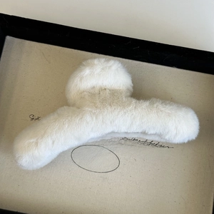 Macro detail of soft beige plush hair claw clip on a minimal wooden display tray