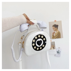 Close-up of a white patent leather crossbody bag in a creative retro telephone shape