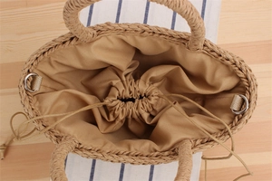 Top view of beige straw handbag featuring a drawstring fabric liner and metal D-rings