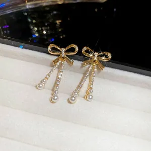 Gold plated bowknot earrings with zircon tassels and hanging pearls on a white velvet tray