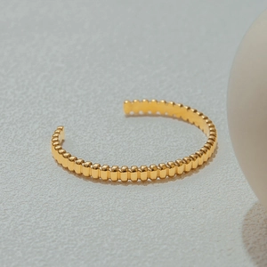 Close-up of golden beaded open bangle with elegant wave texture on gray background
