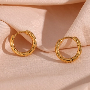 Macro shot of gold hoop earrings with irregular lava texture on soft pink satin