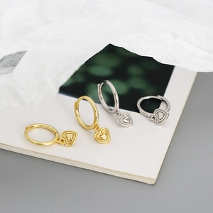 Close-up of gold and silver S925 heart pendant hoop earrings on white texture