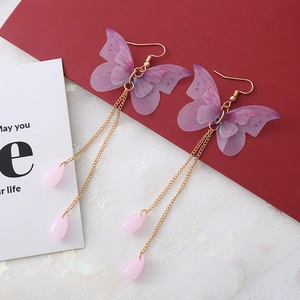 Détail de boucles d'oreilles ailes de papillon avec tulle violet et perles roses