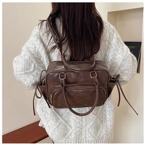 Detail of a dark brown vintage leather backpack on a model wearing a white knit sweater