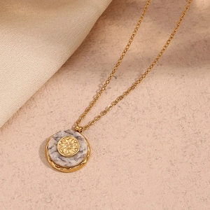 Detailed macro view of 18K gold sunburst necklace with marble stone texture