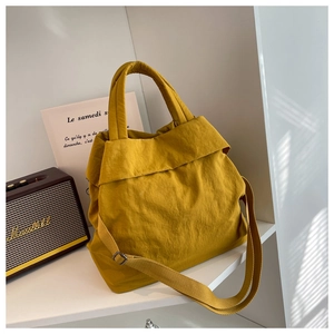 Detail of yellow pleated nylon tote bag with wide strap on a minimalist white shelf