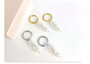 Flat lay of gold and silver C-shaped hoop earrings with white baroque pearl pendants