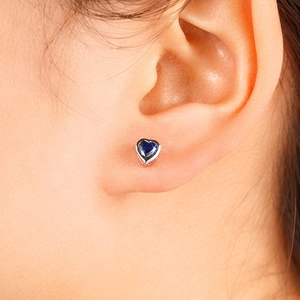 Close-up of a heart-shaped sapphire stud earring with a silver base on a model's ear