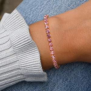 Close-up of a delicate gold tennis bracelet with pink round-cut zircons worn on wrist