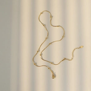Detail of a gold snake chain necklace with beads and a stainless steel lobster clasp