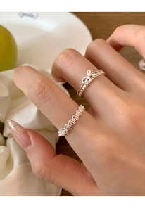 Detailed view of silver bow and pearl open rings worn on hand with elegant lace pattern