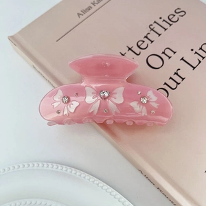 Detailed view of pink translucent butterfly hair claw clip with rhinestones on a book