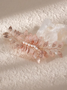 Detail of rose gold bridal hair comb with metal leaves and pearls on textured paper