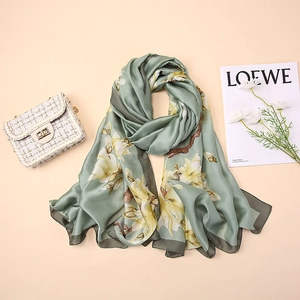 Detail of silk scarf with yellow magnolia print and dark green rolled edges on cream base